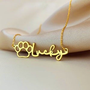 May include: Gold necklace with a paw print charm and the word "Lucky" written in cursive.