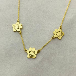 May include: Gold necklace with three paw print charms, each engraved with a name: Neal, Kim, and Phill.