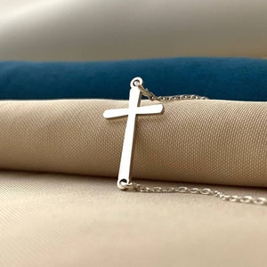 Op de afbeelding: Een zilveren kruis ketting met een delicate hanger. Het kruis is eenvoudig en elegant, met een gladde, gepolijste afwerking.