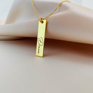 Puede incluir: Collar de oro con un colgante de barra vertical grabado con el nombre "Dianna".