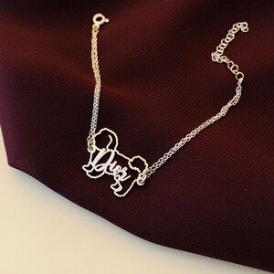 May include: A silver chain bracelet with a silver charm in the shape of a dog. The charm has the word "Dior" written on it.