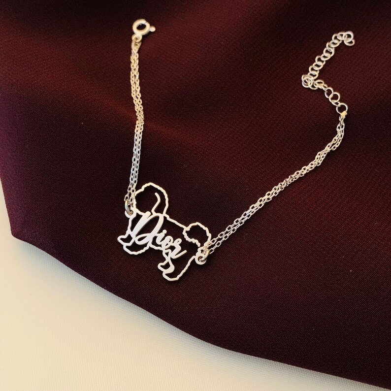May include: A silver chain bracelet with a silver charm in the shape of a dog. The charm has the word "Dior" written on it.