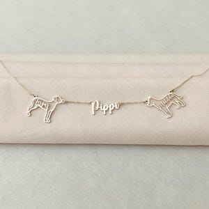 以下が含まれることがあります： 2匹の犬のシルエットがついたシルバーネックレス。1匹は「Tergus」、もう1匹は「Matilda」と名付けられている。ネックレスには中央に「Pippi」という名前のチャームも付いている。