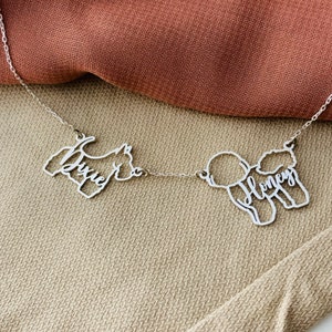May include: A silver necklace with two dog silhouettes, one of a terrier with the name "Dixie" and the other of a poodle with the name "Honey".
