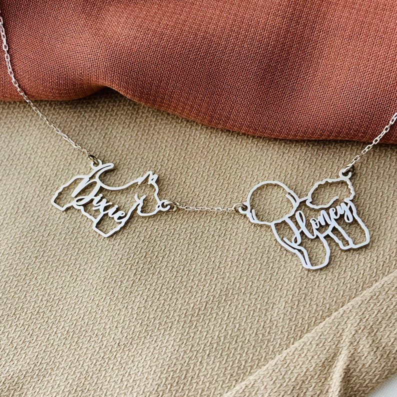 May include: A silver necklace with two dog silhouettes, one of a terrier with the name "Dixie" and the other of a poodle with the name "Honey".