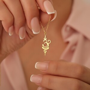 K&ouml;nnte beinhalten: Eine goldene Halskette mit einem zarten Om-Anh&auml;nger. Der Anh&auml;nger ist eine stilisierte Darstellung des Sanskrit-Symbols Om, das ein heiliger Laut im Hinduismus und Buddhismus ist.