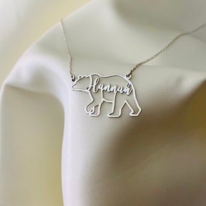 Peut inclure: Collier en argent avec un pendentif en forme d'ours. L'ours est d&eacute;coup&eacute; et le nom "Hannah" est &eacute;crit &agrave; l'int&eacute;rieur de la silhouette de l'ours.