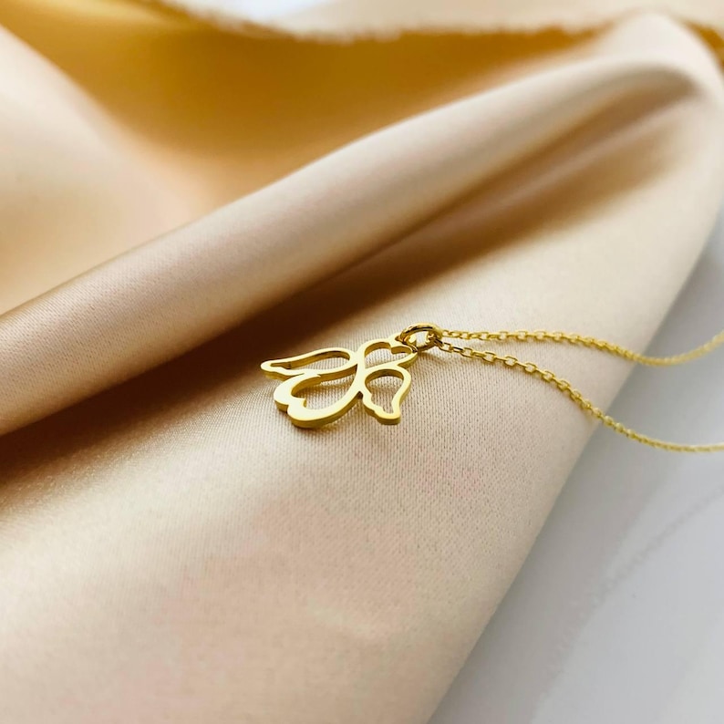 May include: A gold angel pendant necklace on a delicate chain. The pendant is a simple, cutout design of an angel with wings.