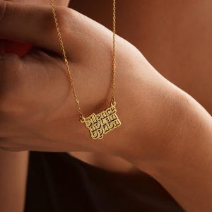 May include: Gold-colored necklace with a rectangular pendant. The pendant features the words "Silence not an option" in a stylized font. The necklace is displayed against a blurred background.