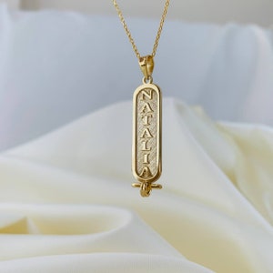 K&ouml;nnte beinhalten: Goldkette mit einem Anh&auml;nger, auf dem der Name "NATALIA" in einer vertikalen, stilisierten Schrift steht.