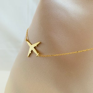 Op de afbeelding: Een gouden vliegtuig hanger ketting met een delicate ketting. De hanger is een eenvoudige silhouet van een vliegtuig.