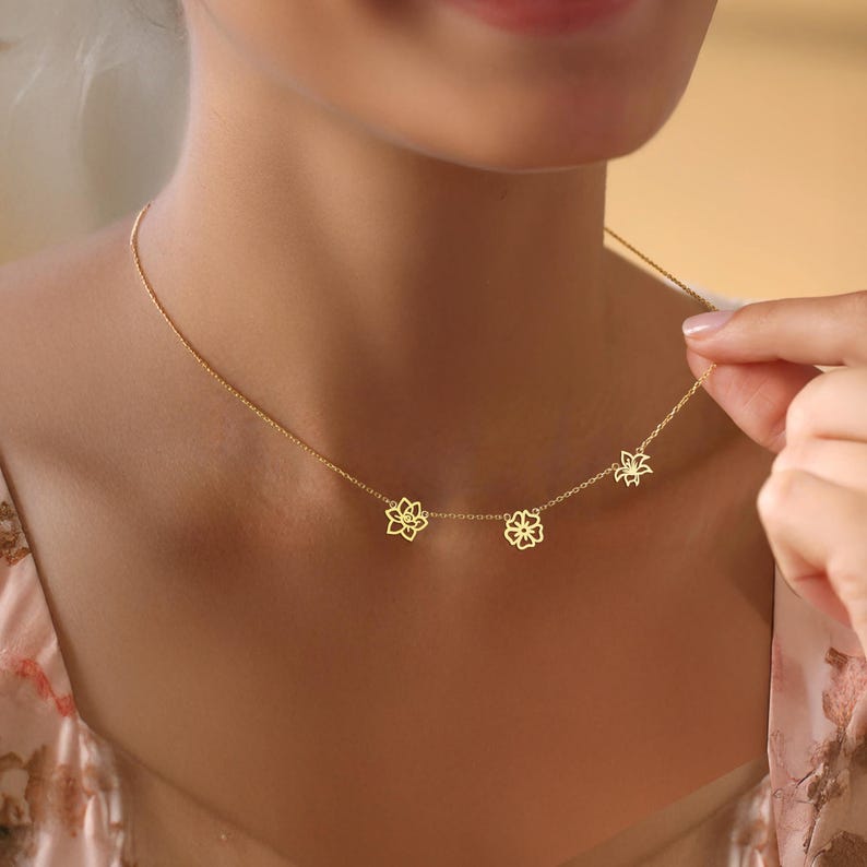 K&ouml;nnte beinhalten: Eine goldene Halskette mit drei zarten Blumenanh&auml;ngern. Die Kette wird von einem Model getragen.