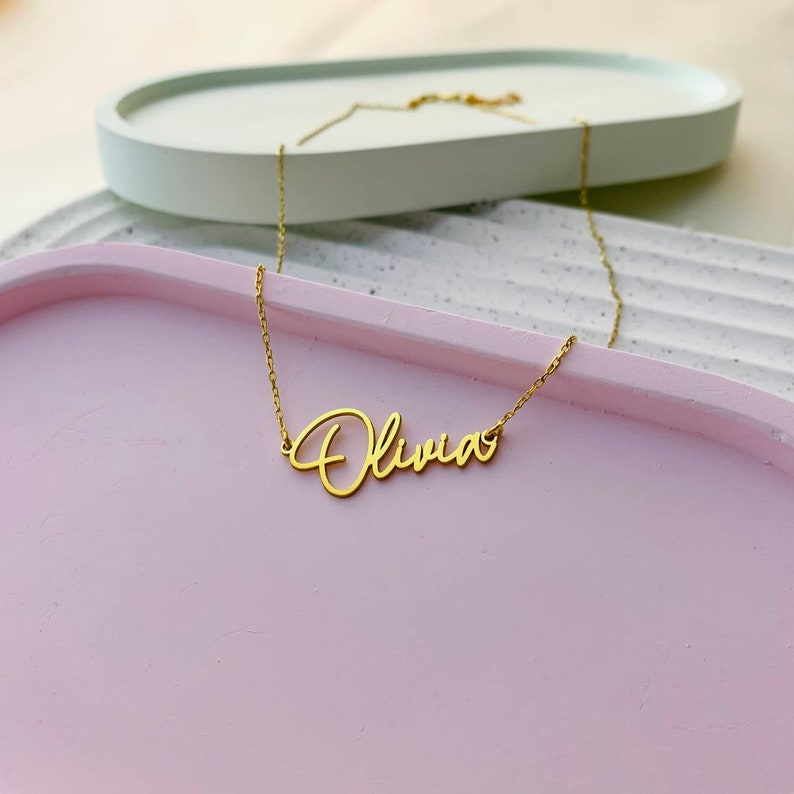 K&ouml;nnte beinhalten: Eine goldene Halskette mit dem Namen "Olivia" in Schreibschrift.