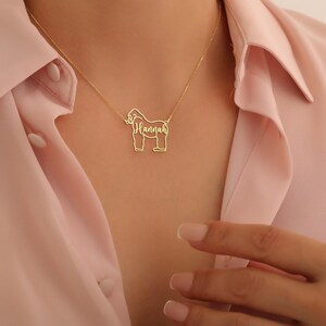 May include: A gold necklace with a gorilla pendant. The gorilla is outlined and the name "Hannah" is written inside the outline.
