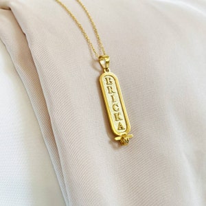 K&ouml;nnte beinhalten: Goldkette mit einem Anh&auml;nger, auf dem "ERRICKA" in einer vertikalen Schriftart im Hieroglyphenstil steht.