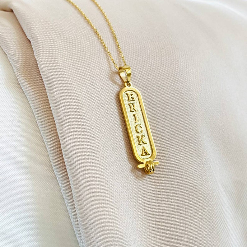 K&ouml;nnte beinhalten: Goldkette mit einem Anh&auml;nger, auf dem "ERRICKA" in einer vertikalen Schriftart im Hieroglyphenstil steht.
