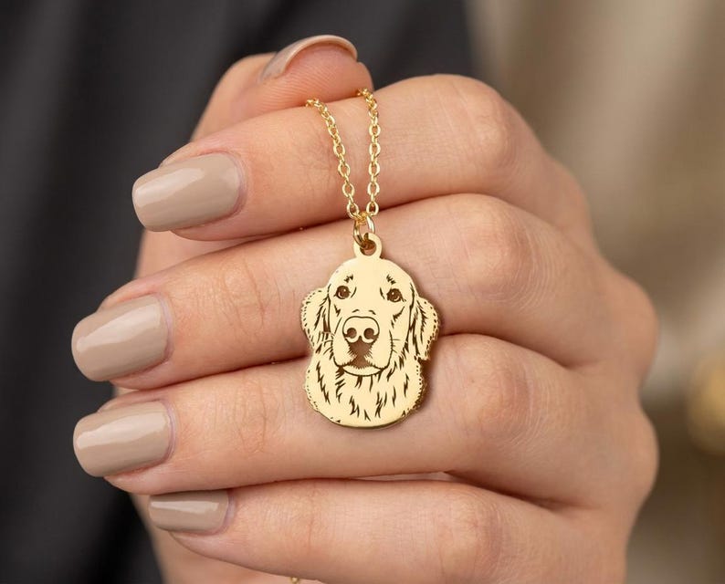 May include: A gold-colored pendant necklace featuring a detailed engraving of a Golden Retriever's head. The pendant hangs from a delicate chain. The dog's features are clearly defined, showcasing its eyes, nose, and fur texture. The necklace is a piece of jewelry.