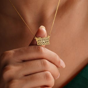 K&ouml;nnte beinhalten: Eine goldfarbene Halskette mit dem Schriftzug "Silence not an option" auf einem rechteckigen Anh&auml;nger. Die Halskette wird von den Fingern einer Person gehalten, wobei die Kette vor einem hautfarbenen Hintergrund sichtbar ist.