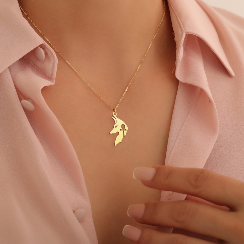 Op de afbeelding: Een gouden ketting met een hanger met een Anubis-silhouet met een ankh erin. De hanger is een uitsnede.