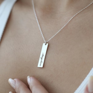 Puede incluir: Un collar de plata con un colgante rectangular que dice "Angelica" en cursiva.
