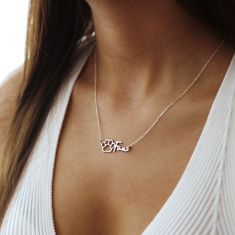 May include: Silver necklace with a paw print charm and the name "Fox" written in cursive.