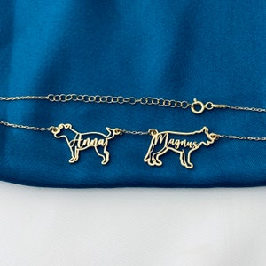 May include: A gold chain necklace with two dog-shaped pendants. The pendants are cut out and the names "Anna" and "Magnus" are written inside the cutouts.