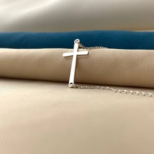 May include: A silver cross pendant necklace on a delicate chain. The cross is simple and elegant, with a smooth finish.