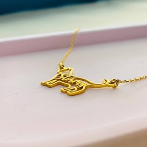 May include: A gold necklace featuring a cat silhouette pendant. The cat's outline is formed by the word "Stormy".