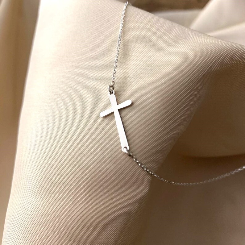 May include: A silver chain necklace with a simple silver cross pendant.