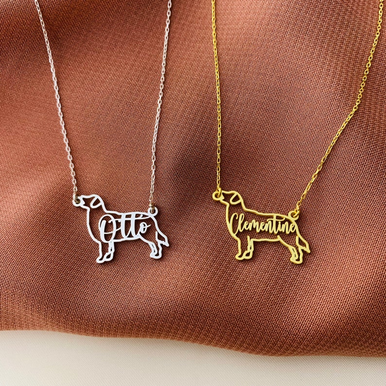 May include: Two silver necklaces with dog silhouettes. One necklace features the name "Otto" and the other features the name "Clementine".