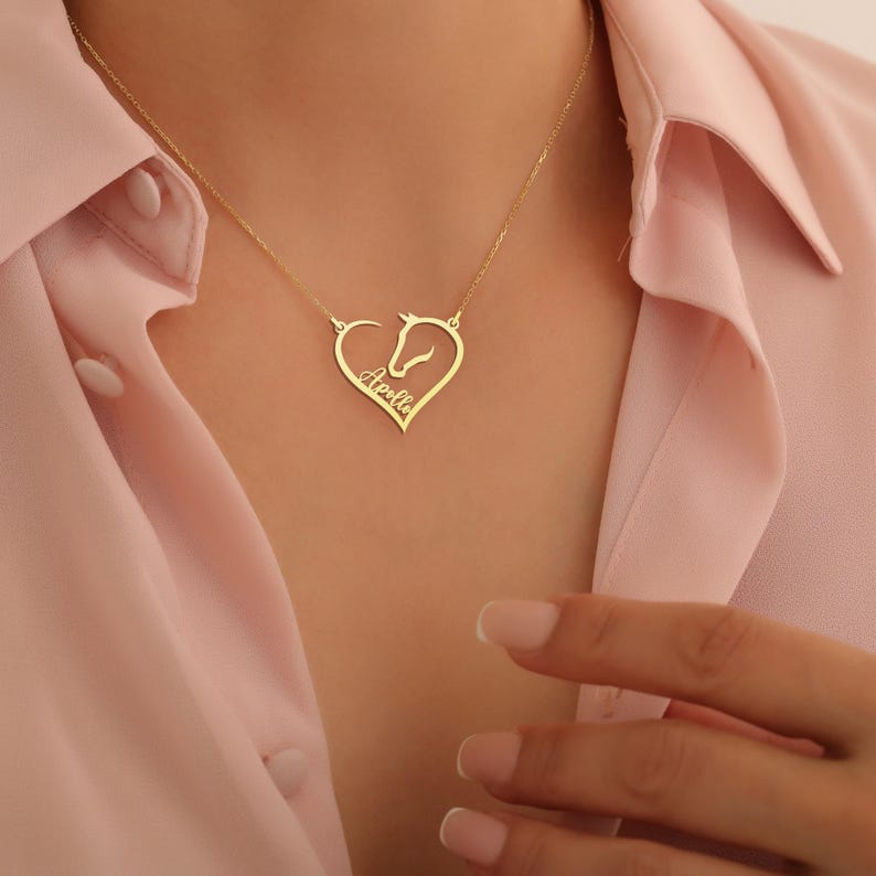K&ouml;nnte beinhalten: Goldkette mit einem herzf&ouml;rmigen Anh&auml;nger, der eine Pferdesilhouette und den Namen "Adelle" im Inneren tr&auml;gt.
