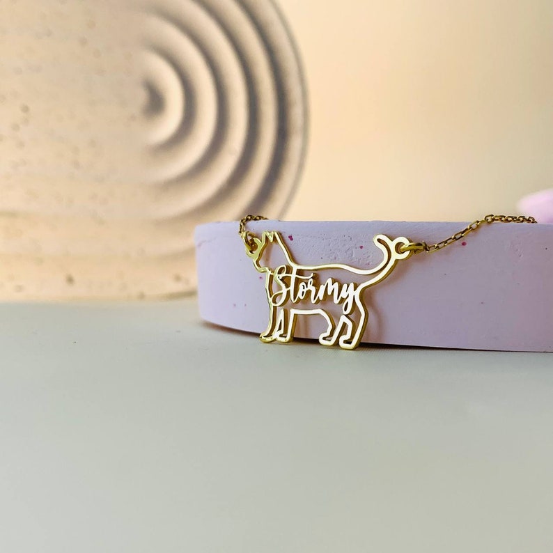 May include: Gold necklace featuring a cat silhouette pendant. The cat's name, "Stormy", is inscribed within the silhouette.
