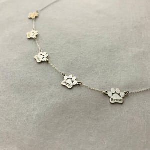 May include: Silver necklace with five paw print charms, each engraved with a different name: Sophie, Jupie, Bowser.