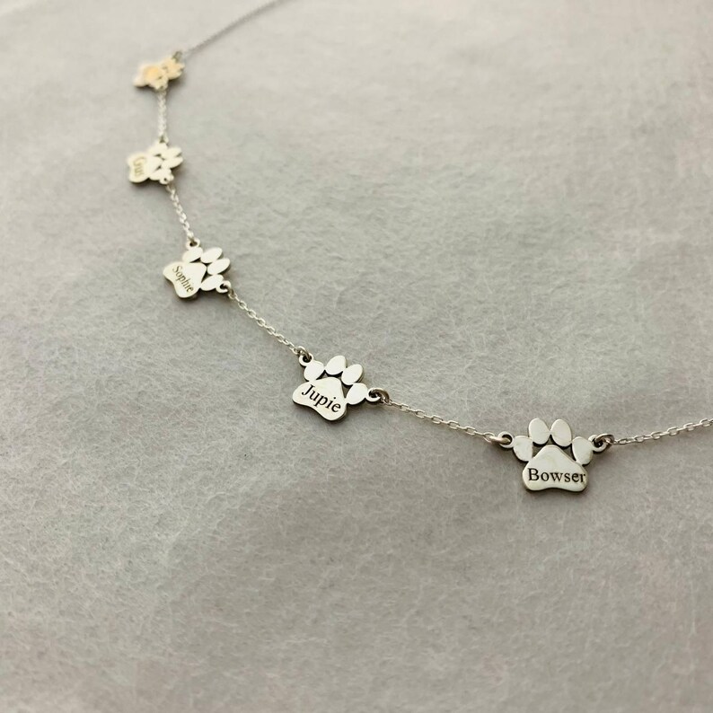 May include: Silver necklace with five paw print charms, each engraved with a different name: Sophie, Jupie, Bowser.
