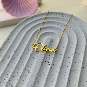 K&ouml;nnte beinhalten: Eine goldene Halskette mit dem Namen "Olivia" in Schreibschrift.