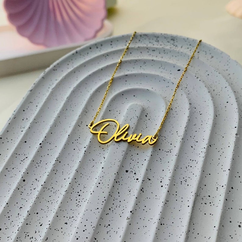 K&ouml;nnte beinhalten: Eine goldene Halskette mit dem Namen "Olivia" in Schreibschrift.
