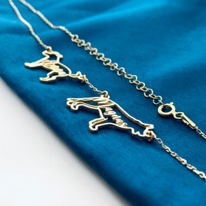 May include: A gold chain necklace with two dog silhouette charms. The chain is delicate and the charms are detailed.