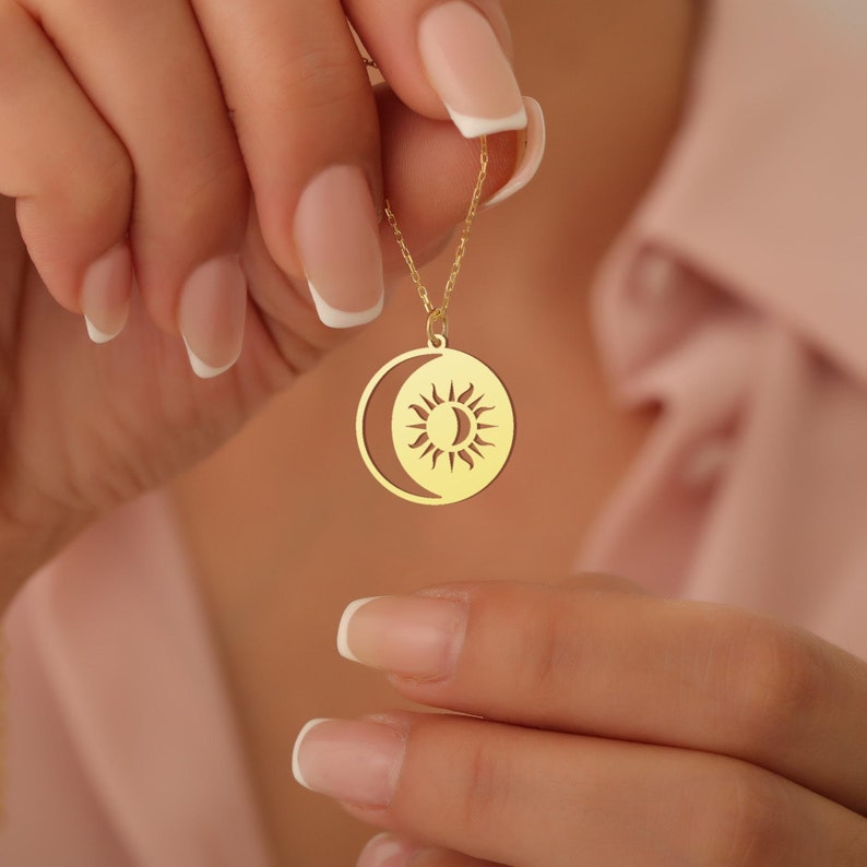 May include: A gold necklace featuring a sun and moon pendant. The pendant is a circular design with a crescent moon on one side and a sun with rays on the other.