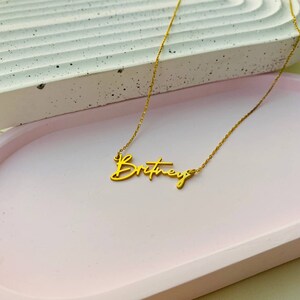 May include: Gold necklace with the name "Britney" written in cursive script.