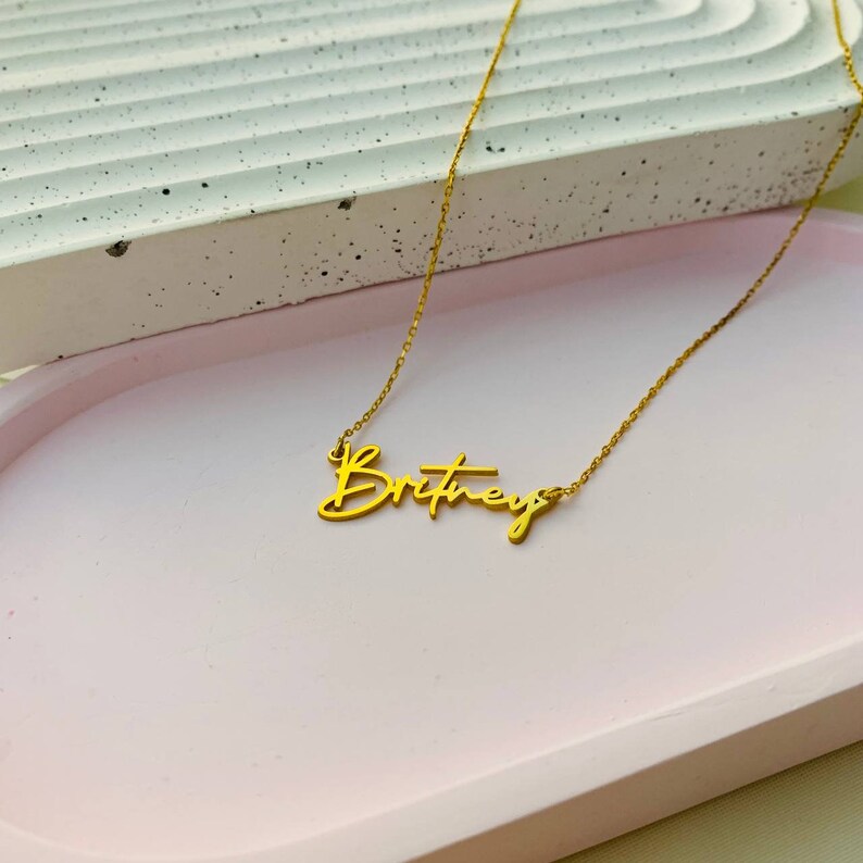 May include: Gold necklace with the name "Britney" written in cursive script.