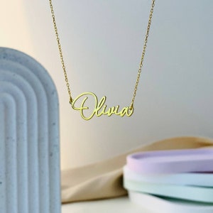 K&ouml;nnte beinhalten: Eine goldene Halskette mit dem Namen "Olivia" in Schreibschrift.