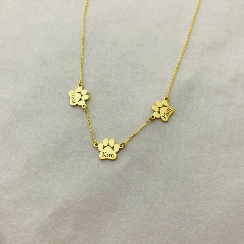 May include: Gold necklace with three paw print charms, each engraved with a name: Neal, Kim, and Phill.