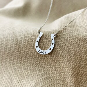 以下が含まれることがあります： 馬蹄の形をしたシルバーネックレス。馬蹄に「Lady」という文字が刻まれています。