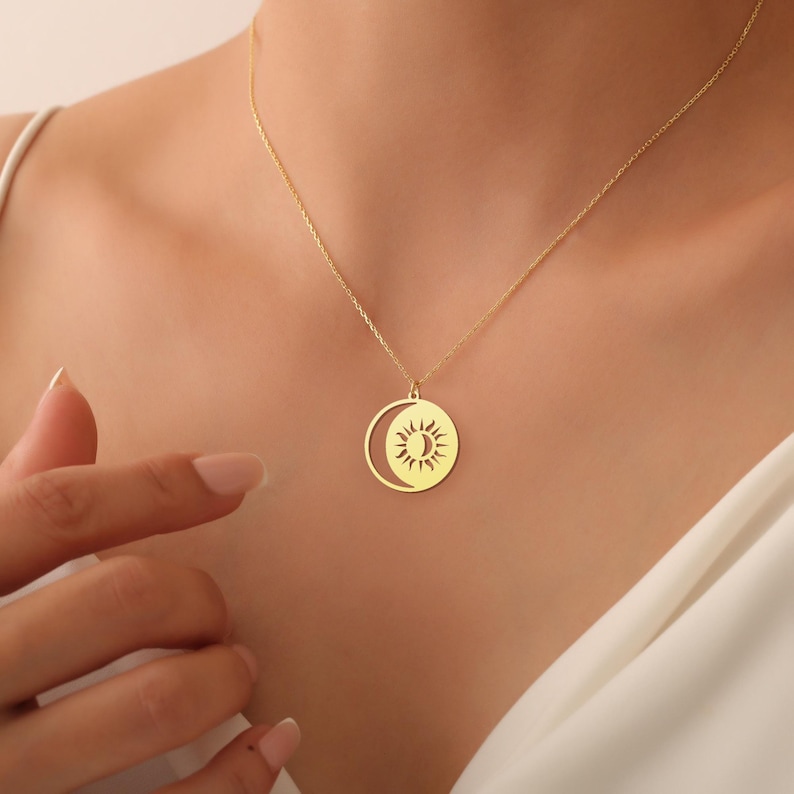 May include: A gold necklace featuring a sun and moon pendant. The pendant is a circular design with a crescent moon cut out, and the sun is positioned within the moon.