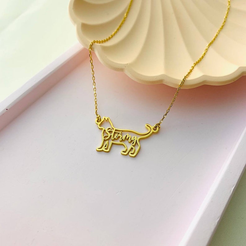 May include: Gold necklace featuring a cat silhouette pendant. The cat's name, "Stormy", is inscribed within the silhouette.