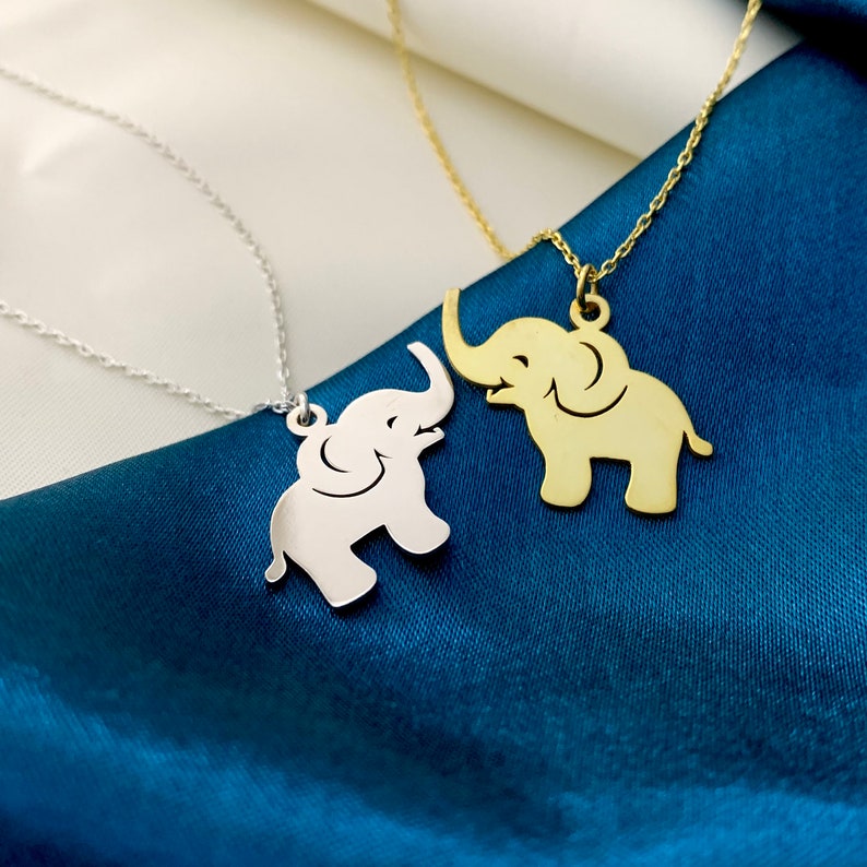 Puede incluir: Dos collares de plata con colgantes de elefante. Un elefante es de oro y el otro de plata.