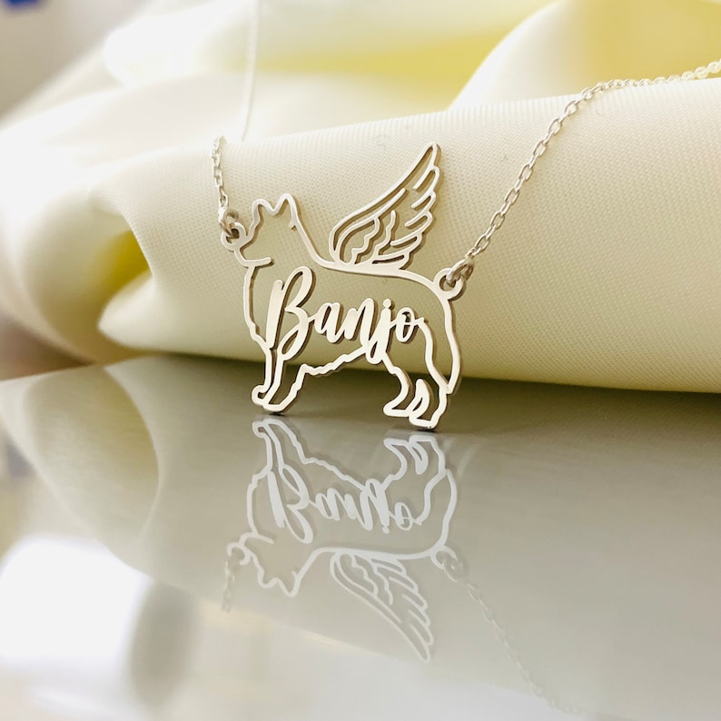 May include: Silver necklace with a dog silhouette and wings. The dog's name, "Banjo", is written on the pendant.