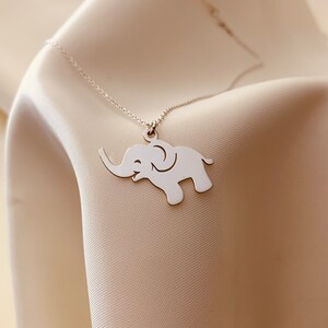 Puede incluir: Un collar de plata con un delicado colgante de elefante. El elefante est&aacute; mirando hacia la derecha y tiene la trompa levantada.