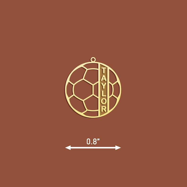 Op de afbeelding: Gouden metalen voetbal ornament met de naam "TAYLOR" verticaal aan de zijkant gegraveerd. Het ornament is 0,8 inch in diameter.