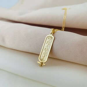 K&ouml;nnte beinhalten: Goldkette mit einem Anh&auml;nger, auf dem "NATALIA" in einer vertikalen, stilisierten Schrift steht. Der Anh&auml;nger ist in Form einer alten &auml;gyptischen Kartusche gestaltet.